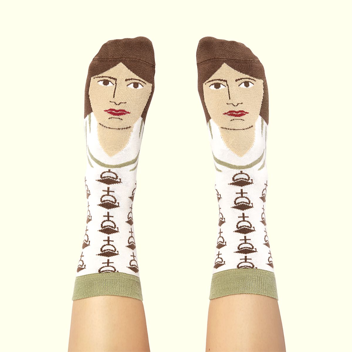 A pair of socks worn on feet, featuring a stylized portrait of a woman with brown hair, beige skin tones, and red lips, with a repeating brown cloche pattern on a white background and olive green cuffs.