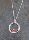 Image of a circular pendant depicting 5 poppies and inscribed with the words Lest We Forget