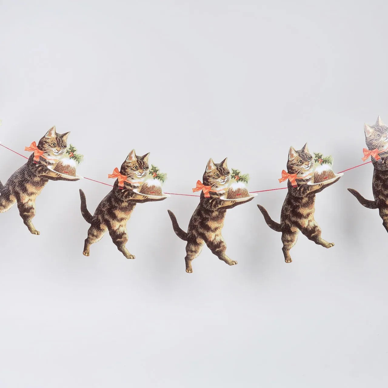 Cats holding a string with a small Christmas tree on a light gray background