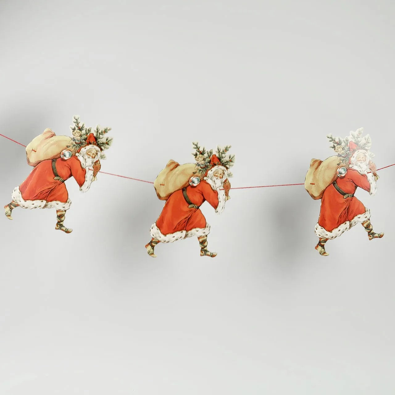 Three decorative figures of Santa Claus on a string against a light gray background