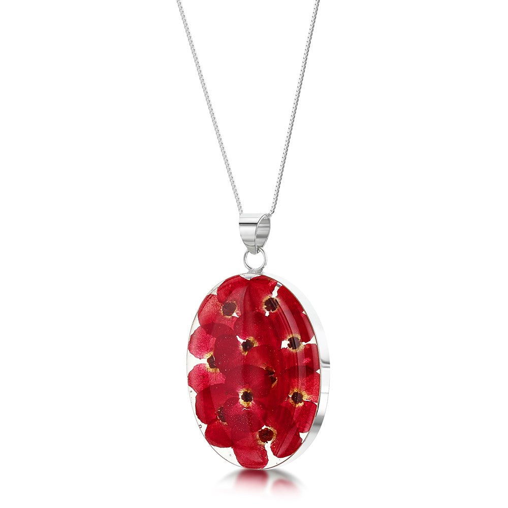 An oval pendant necklace featuring red pressed flowers encased in clear resin, suspended from a silver chain on a white background.