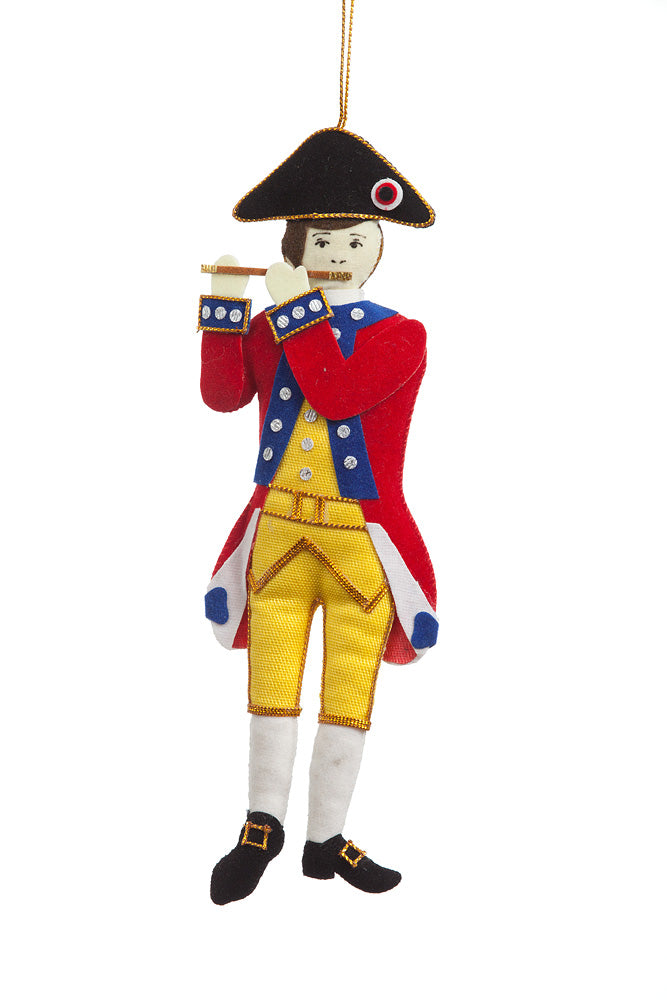 Decorative fabric ornament of a historical figure in red coat and yellow pants on a white background