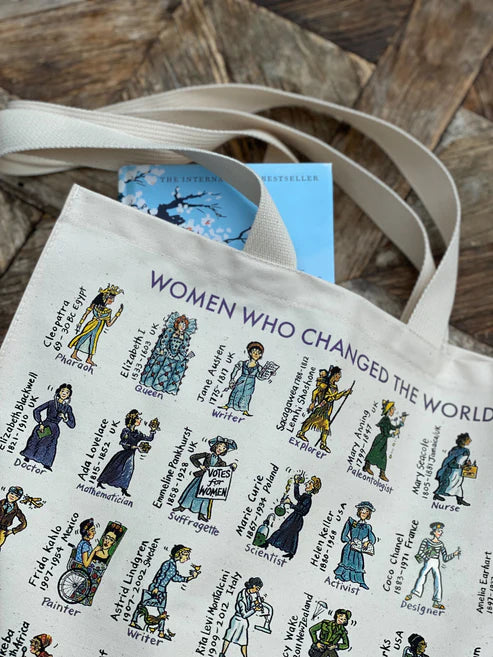 Tote bag with illustrated women and a book inside on a wooden surface