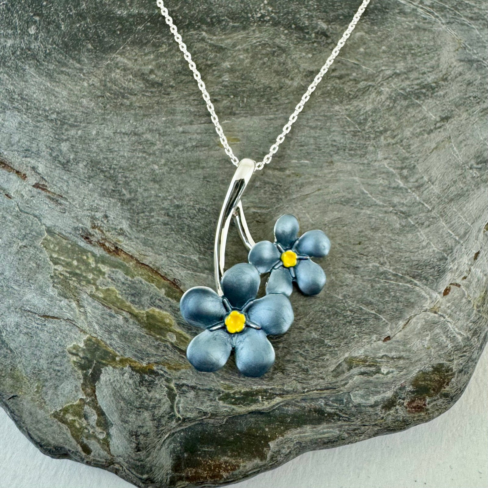 Forget me not shaped pendant with 2 flowers laying on a stone for display