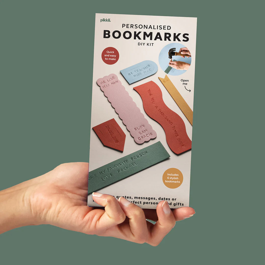 Hand holding a package of personalized bookmarks DIY kit with colorful bookmarks on a green background